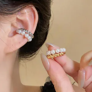 Close-up detail of a double-layer pearl and gold twisted ear cuff held between fingers.