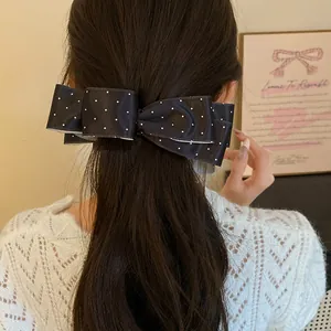 Détail d'un nœud en satin noir à pois porté comme pince dans de longs cheveux foncés