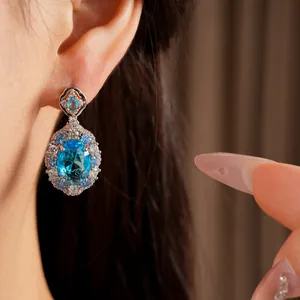 Close-up view of an elegant oval blue zircon drop earring with sparkling accents on model's ear
