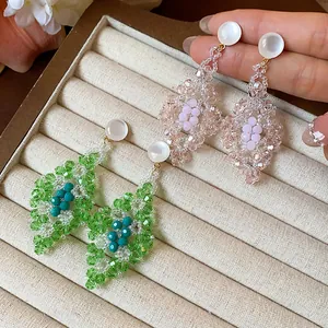 Detalle de pendientes artesanales con forma de rombo hechos con cuentas de vidrio verde y rosa.