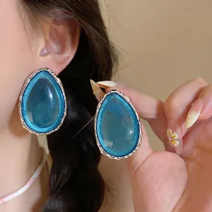 Primo piano di orecchini a goccia in resina blu vibrante con bordi in metallo su una modella.