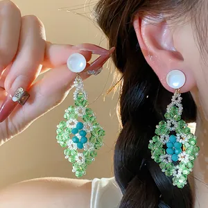 Detalle de pendientes de cuentas verdes y azules con elegante diseño de rombo.