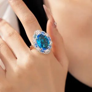 Close-up of an elegant oval blue zircon ring worn on a finger with diamond accents.