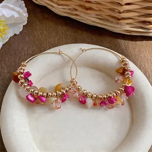 Dettaglio di orecchini a cerchio boho con pietre rosa e arancioni di forma irregolare.
