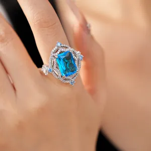 Close-up of a luxury silver ring with a large emerald-cut blue gemstone on a finger.