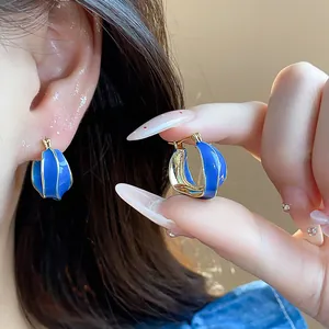 Close-up of blue enamel 14k gold plated irregular hoop earrings on ear and hand