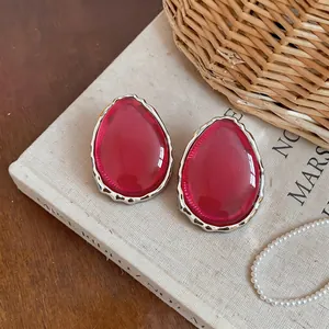 Dettaglio degli orecchini a goccia in resina rosa con cornice d'argento ondulata.