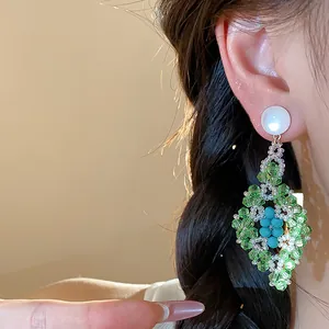 Detalle de pendientes colgantes de cristal verde en forma de rombo estilo bosque