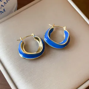 Close-up of irregular 14k gold plated hoop earrings featuring vibrant blue enamel inlay