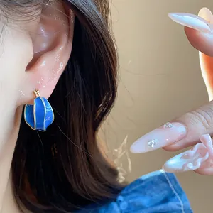 Close-up of a 14k gold plated earring with minimalist irregular blue enamel drip design