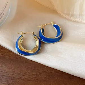 Close-up of irregular 14k gold-plated hoop earrings with vibrant blue enamel details.