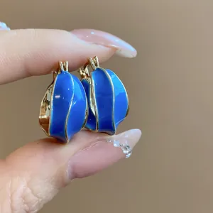 Detailed close-up view of irregular 14k gold plated huggie earrings with vibrant blue enamel