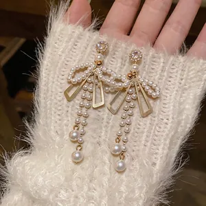 Boucles d'oreilles nœud dorées avec perles et cristaux et de longs pompons fins.