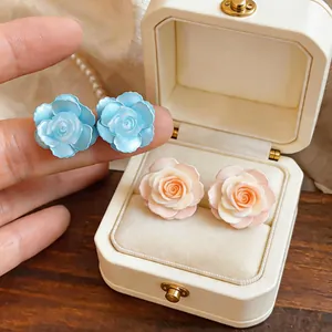 Close-up detail of elegant camellia flower stud earrings in light blue and peach tones.