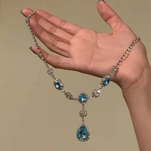 Detailopname van een blauwe kristallen ketting met strass in de hand.
