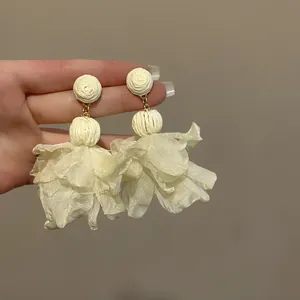 Detail von weißen Netzblüten-Quastenohrringen mit gewebten Perlen in der Hand.