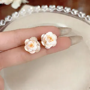 Detailed macro shot of elegant cream and peach camellia flower stud earrings on fingers