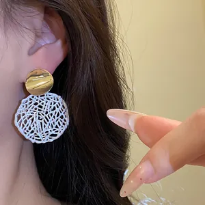 Nahaufnahme von goldenen und weißen hohlen geometrischen Tropfenohrringen im Vintage-Stil