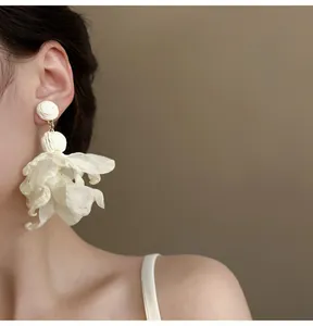 Nahaufnahme eines weißen Netz-Blumenohrrings an einem Model, das zarte Details zeigt.