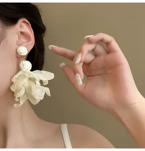 Nahaufnahme von eleganten weißen Netz-Blumen-Quastenohrringen, die ein weibliches Model trägt
