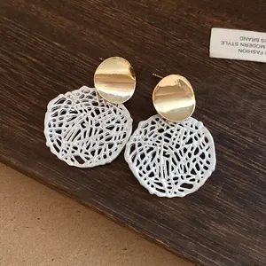Nahaufnahme von Vintage-Ohrsteckern mit weißem filigranem Hohlanhänger-Detail auf Holz