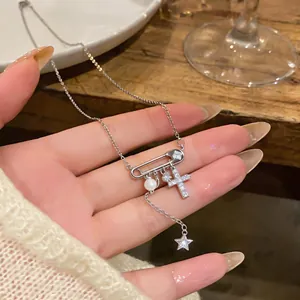Primo piano della collana a spilla con zirconi, ciondoli a croce, stella e perla.