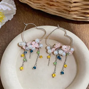 Heart-shaped hoop earrings featuring pearls and colorful flower tassels on a tray