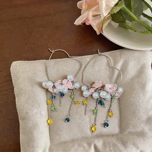 Detail view of heart-shaped earrings with pearls, pink flowers and colorful beaded tassels.