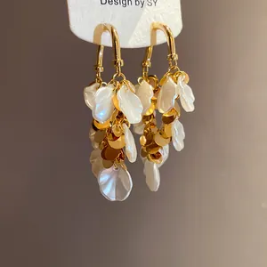 Gros plan de pompons élégants en pétales de nacre et disques dorés sur boucles d'oreilles