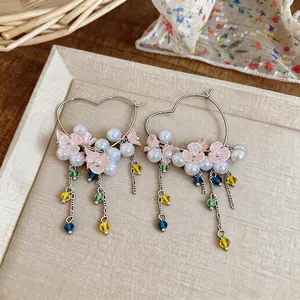 Close-up of heart-shaped hoop earrings featuring pink flowers and colorful tassels