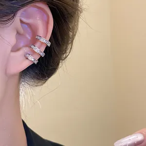 Macro view of three clear zircon-inlaid silver ear cuffs worn on model ear helix