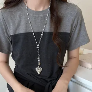 Detail of a French style long pearl necklace with a large heart pendant worn by a model