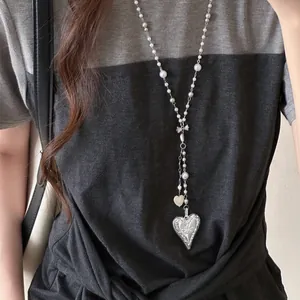 Detailed view of an elegant long pearl necklace featuring a large engraved silver heart pendant