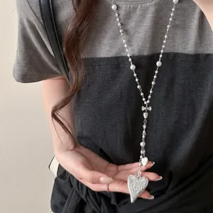 Detail view of a long pearl necklace with bow and heart pendant worn by model.