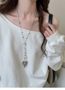 Detail view of a long French style pearl necklace with a vintage heart pendant worn.