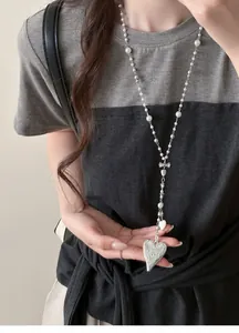 Detailed view of a long pearl necklace with a vintage silver heart pendant on a model