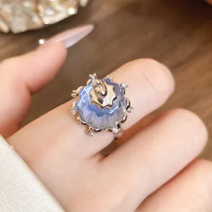 Close-up of a light blue resin pudding-shaped ring with zircon accents on a finger