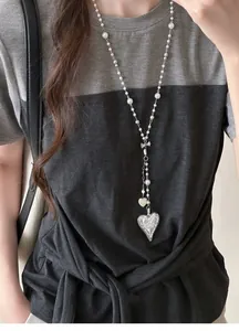 Detailed view of a French style long necklace with pearls and a heart pendant on a model