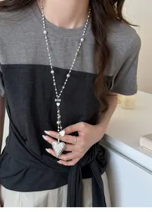 Close-up of elegant long pearl necklace with ornate silver heart pendant on model