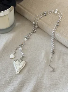 Detail of a French style pearl necklace featuring an elegant silver heart-shaped locket pendant