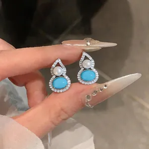 Close-up of gourd-shaped stud earrings with turquoise and pearl accents