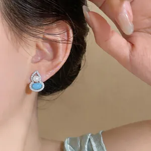 Close-up of elegant gourd-shaped earring with blue stone and pearl on ear
