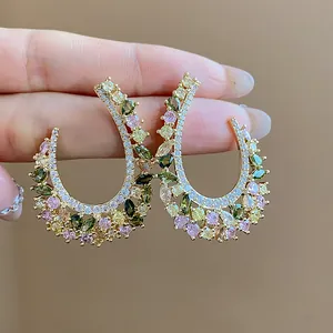 Primo piano dettagliato di orecchini a C dorati con pietre di zircone multicolore vivaci.