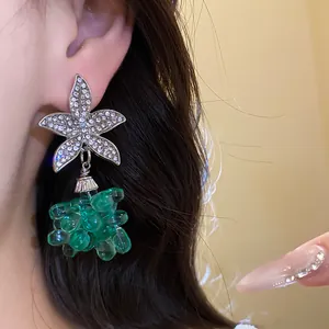 Nahaufnahme eines glitzernden silbernen Blumenohrrings mit smaragdgrünen Perlenanhängern.