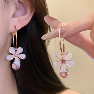 Close-up of rose gold hoop earrings with white resin flowers and pink crystal drops