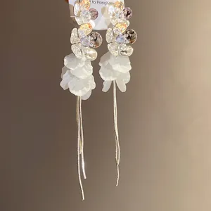 Gros plan sur d'élégantes boucles d'oreilles pétales en résine blanche et longs glands