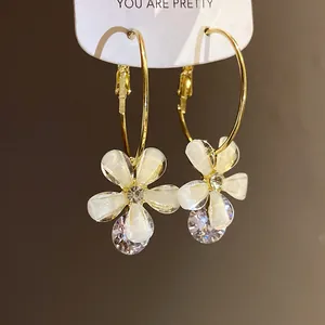 Close-up of elegant gold hoop earrings with white resin flowers and sparkling zircons