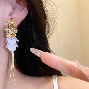 Détail de boucles d'oreilles fleurs dorées avec pétales en résine blanche et glands