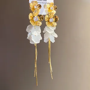 Gros plan de boucles d'oreilles fleurs dorées avec pétales en résine et longues franges