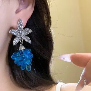 Detailaufnahme eines silbernen Strassblumen-Ohrrings mit blauen Glasperlen in Traubenform